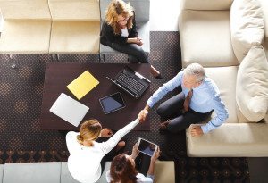 From above image of business people make a deal and shaking hands while sitting at meeting.