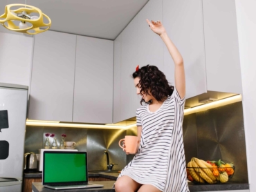 Happy morning in kitchen in modern apartment of joyful young woman in dress having fun on table. Laptop with green screen, tea, brightful emotions, smiling, true emotions