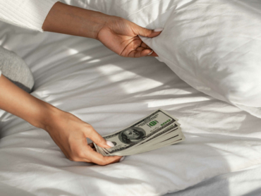 Closeup of unrecognizable millennial African American woman hiding money under pillow at home. Wealth, Financial Safety And Literacy, Distrust In Banking Services Concept.