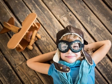 Child pilot with vintage plane toy on grunge wooden background