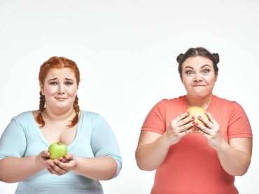 Funny picture of amusing chubby women on white background. One woman holding a sandwich, the other holding an apple.