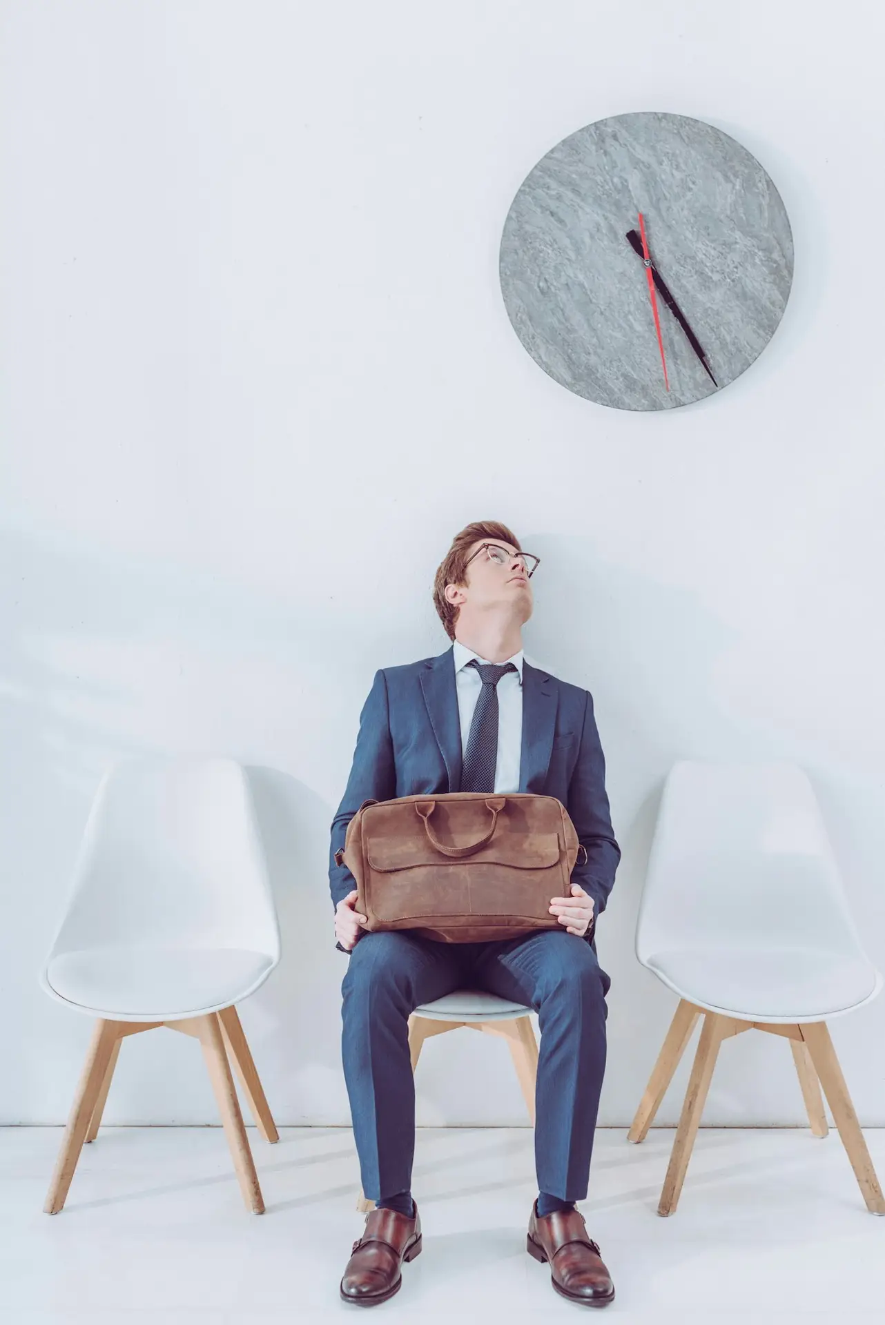 handsome employee in glasses holding briefcase and looking at clock