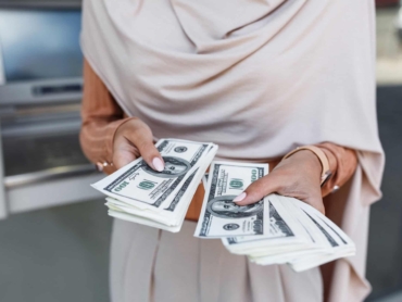 Finance, money transfer, banking, ATM, modern technology, win, withdraw, currency and social distancing. Young unrecognizable arab female in hijab holding a lot of dollars, counting cash, close up