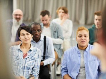 Group of content curious people in casual clothing sitting on chairs and listening to speaker during conference