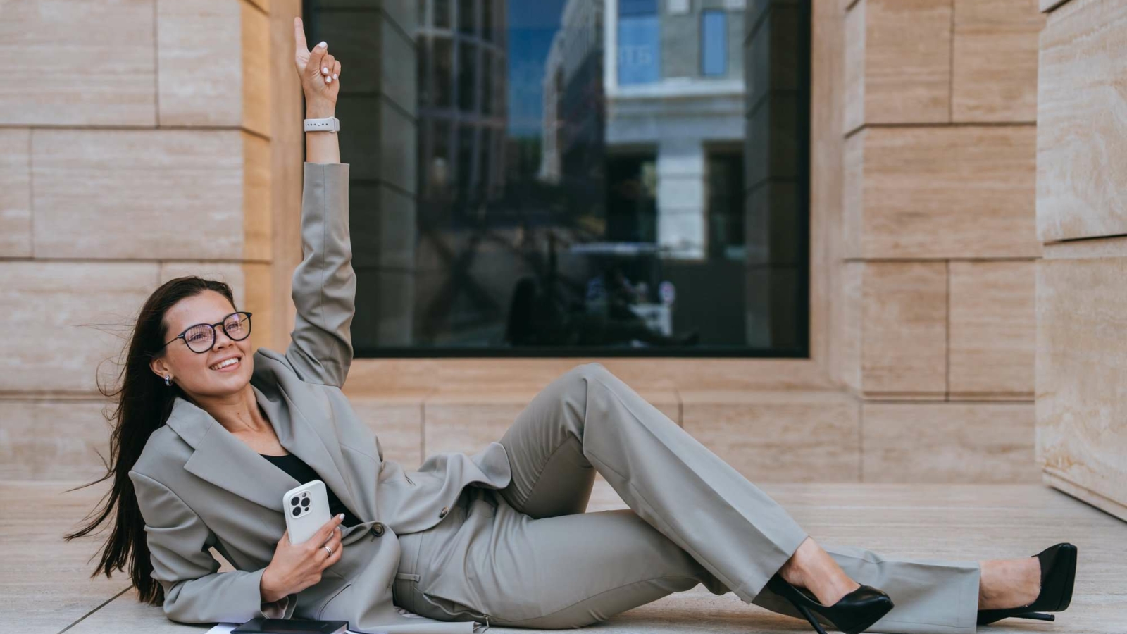 Successful businesswoman in suit laying on building balcony rising finger up celebrating success