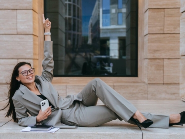 Successful businesswoman in suit laying on building balcony rising finger up celebrating success