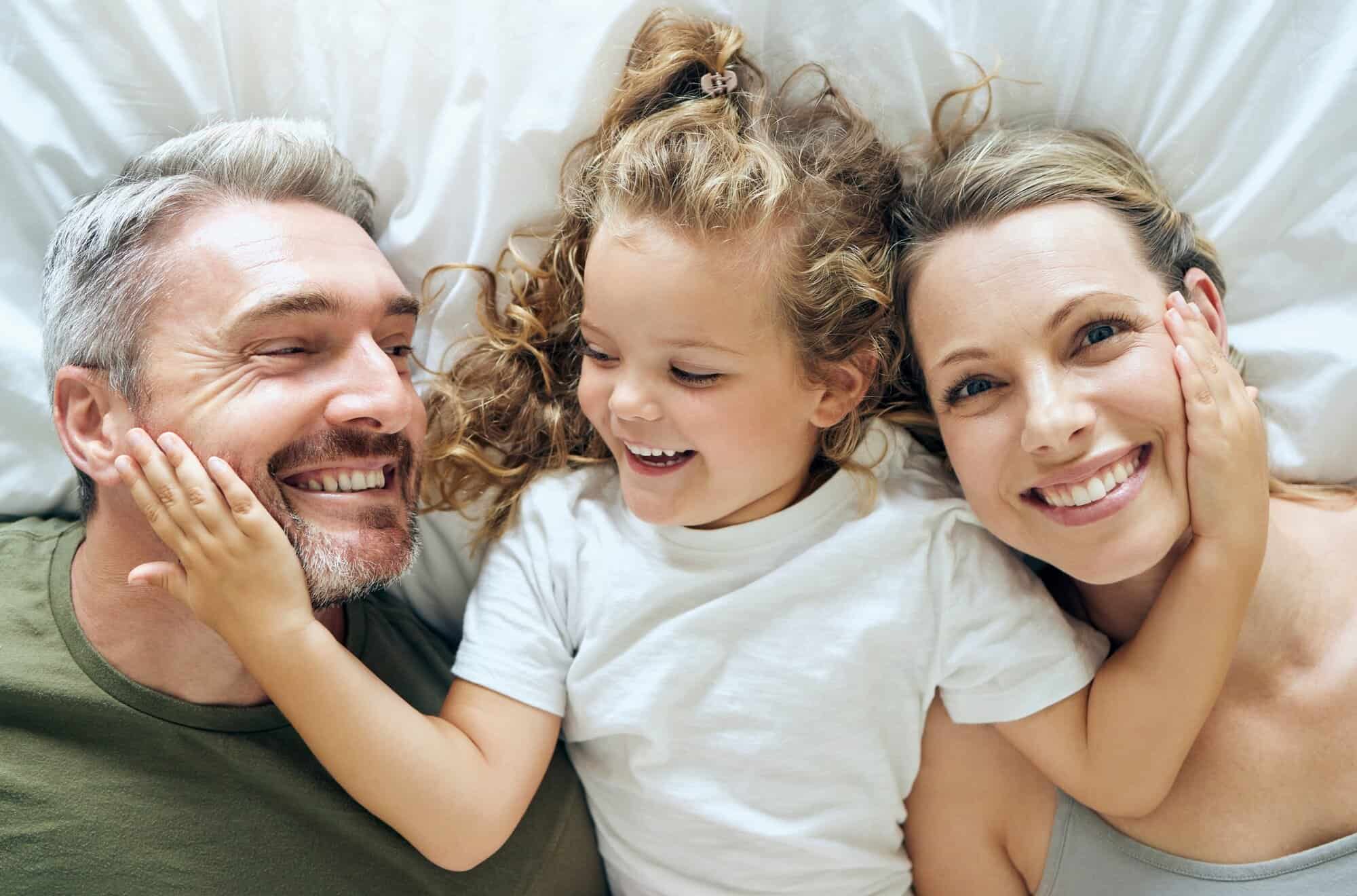 Family, happy and smile of people in bed at home feeling relax in a bedroom bonding. Mother, girl a