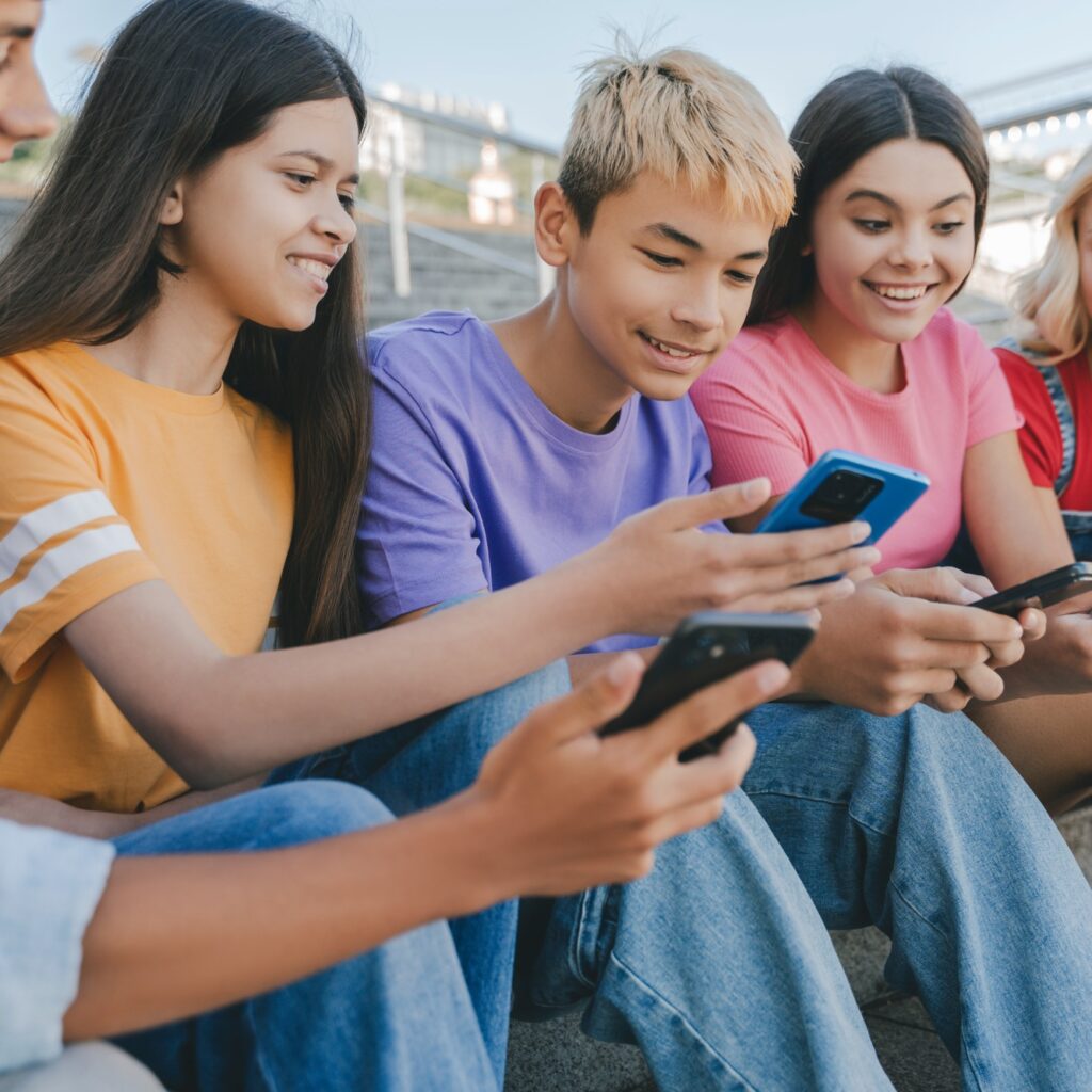 Group of smiling friends, multiracial teenagers holding mobile phones playing mobile game