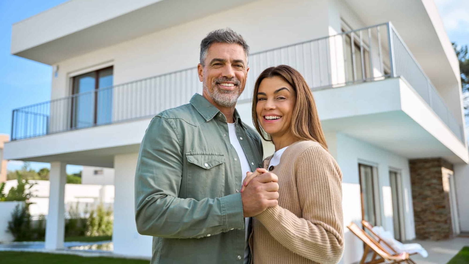 Portrait of happy mature family couple property owners standing outside house.