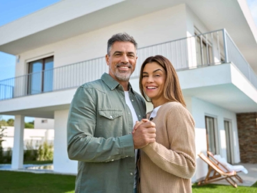 Portrait of happy mature family couple property owners standing outside house.