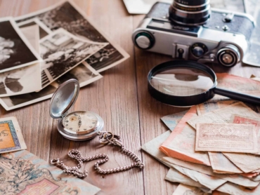 A watch on a chain, aged ruble bills, a film camera and black and white photographs on a wooden table. Vintage collection and nostalgia for the past