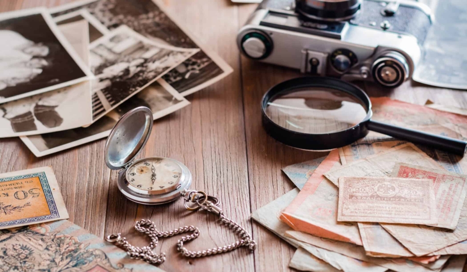 A watch on a chain, aged ruble bills, a film camera and black and white photographs on a wooden table. Vintage collection and nostalgia for the past
