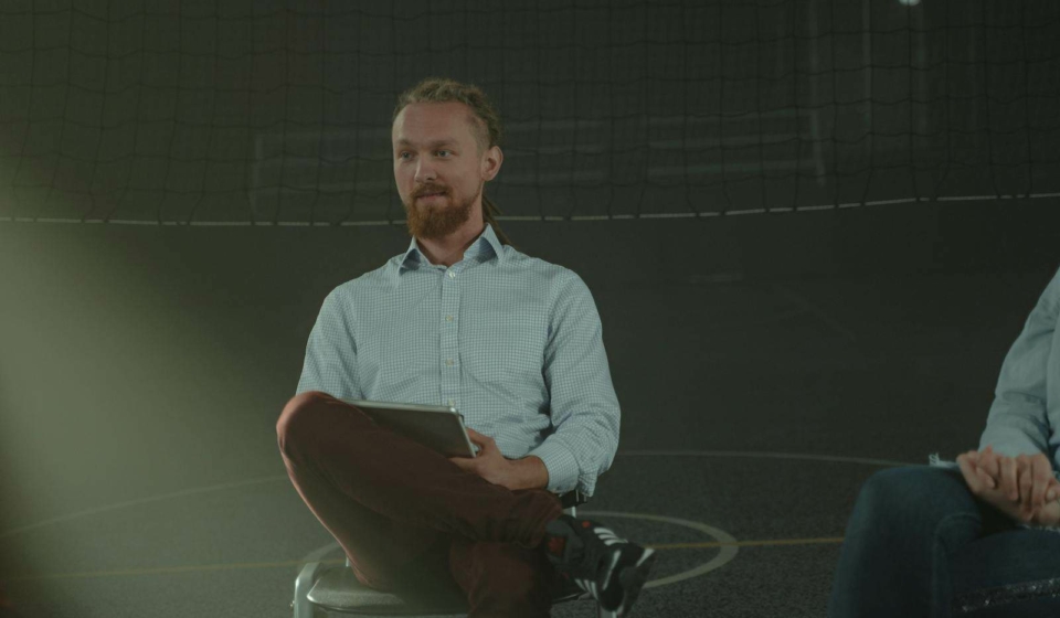 A man holds a meeting in a dimly lit room, engaging with others in a discussion.