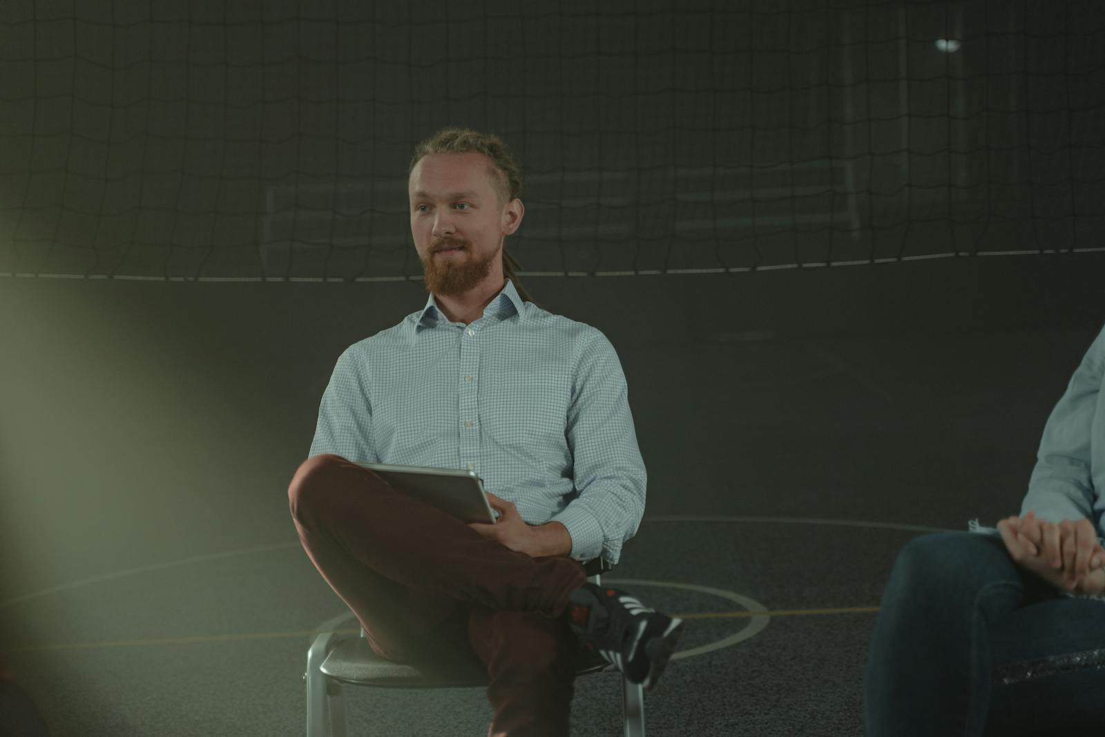 A man holds a meeting in a dimly lit room, engaging with others in a discussion.