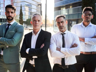 Four confident business men standing outdoors building offices looking at camera and crossing arms.