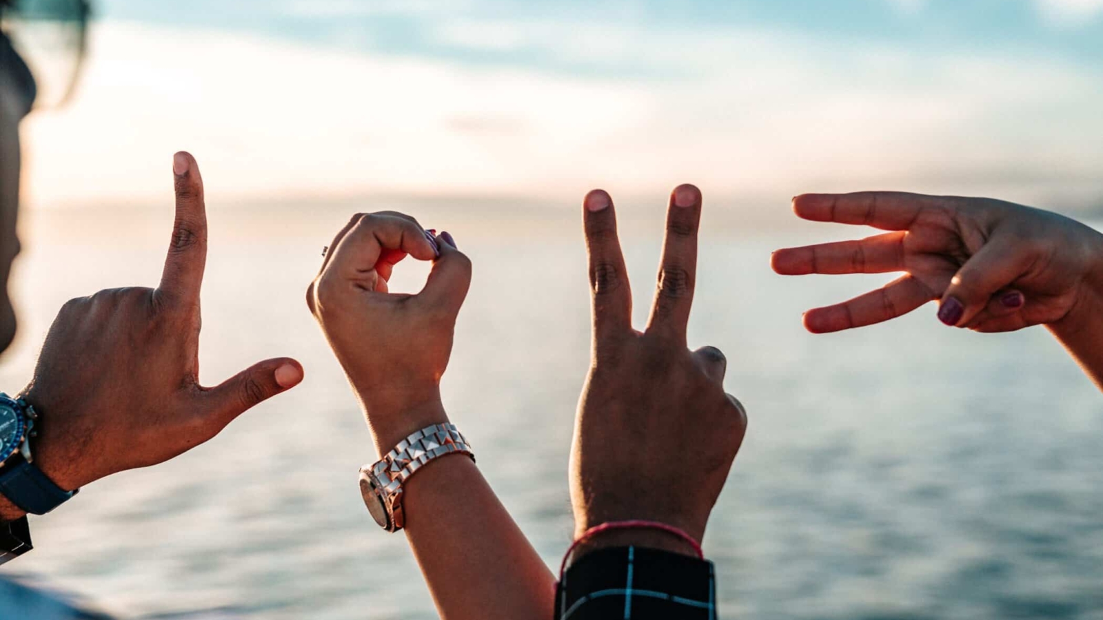 Fingers of a group of friends forming letters that spell "LOVE" on a beautiful natural background of the sea