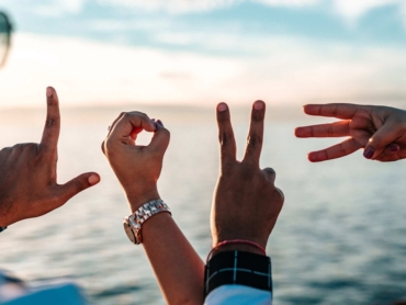 Fingers of a group of friends forming letters that spell "LOVE" on a beautiful natural background of the sea